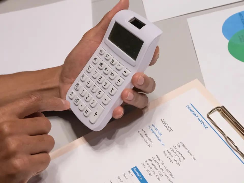 Hands working a calculator beside a printed invoice