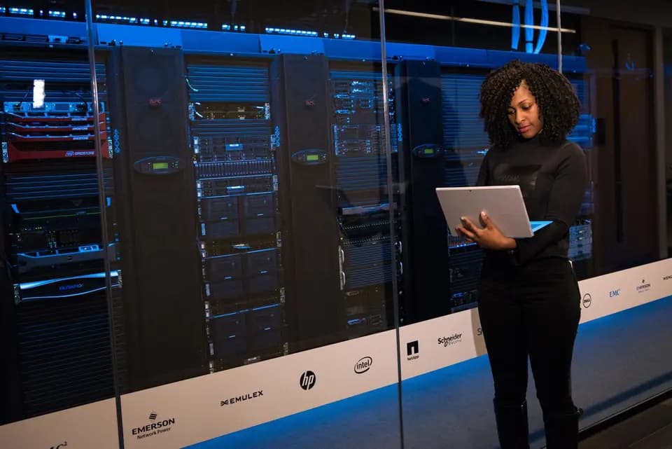 An engineer with a laptop working beside rows of server racks