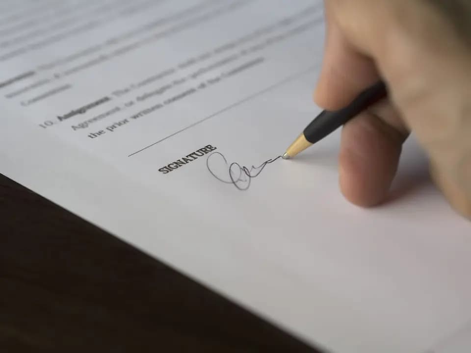 A formal contract being signed on a wooden desk