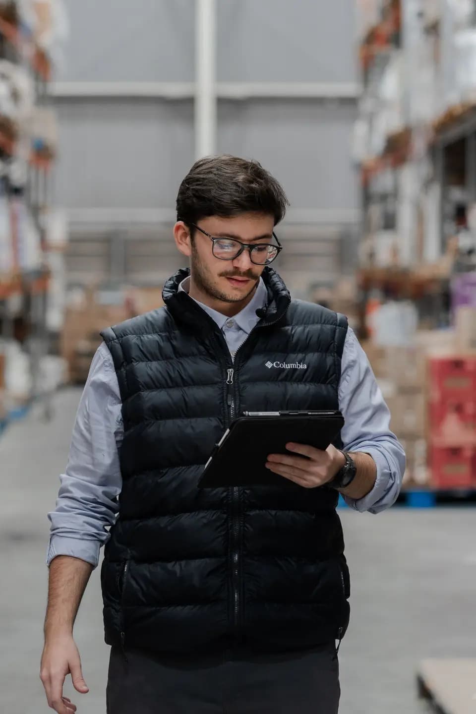 A warehouse worker checking inventory on a tablet beside stacked boxes